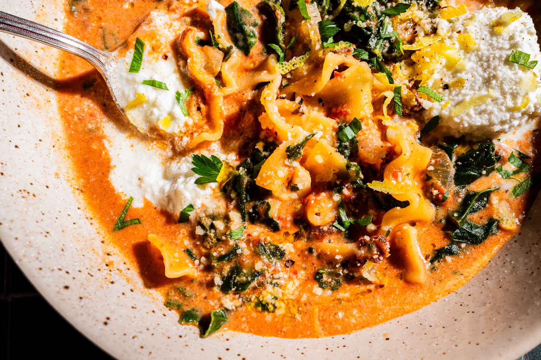 A close-up of marry me lasagna soup with ricotta cheese, pasta sheets, tomato broth, herbs, and greens, served in a shallow bowl with a spoon.