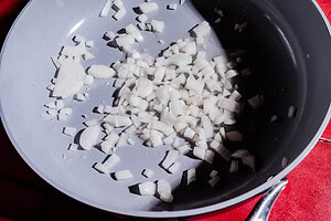 Chopped white onions in a gray frying pan, placed on a red surface, ready to be added to a flavorful purple sweet potato curry.