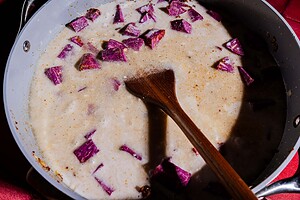 A saucepan filled with milk and chunks of purple sweet potato, stirred with a wooden spatula, creates the perfect base for a vibrant purple sweet potato curry.