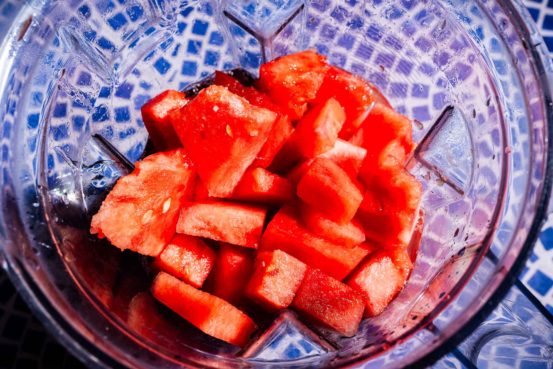 Cubed pieces of watermelon for refreshing watermelon agua fresca inside a blender, viewed from above, on a blue and white mosaic-patterned surface.