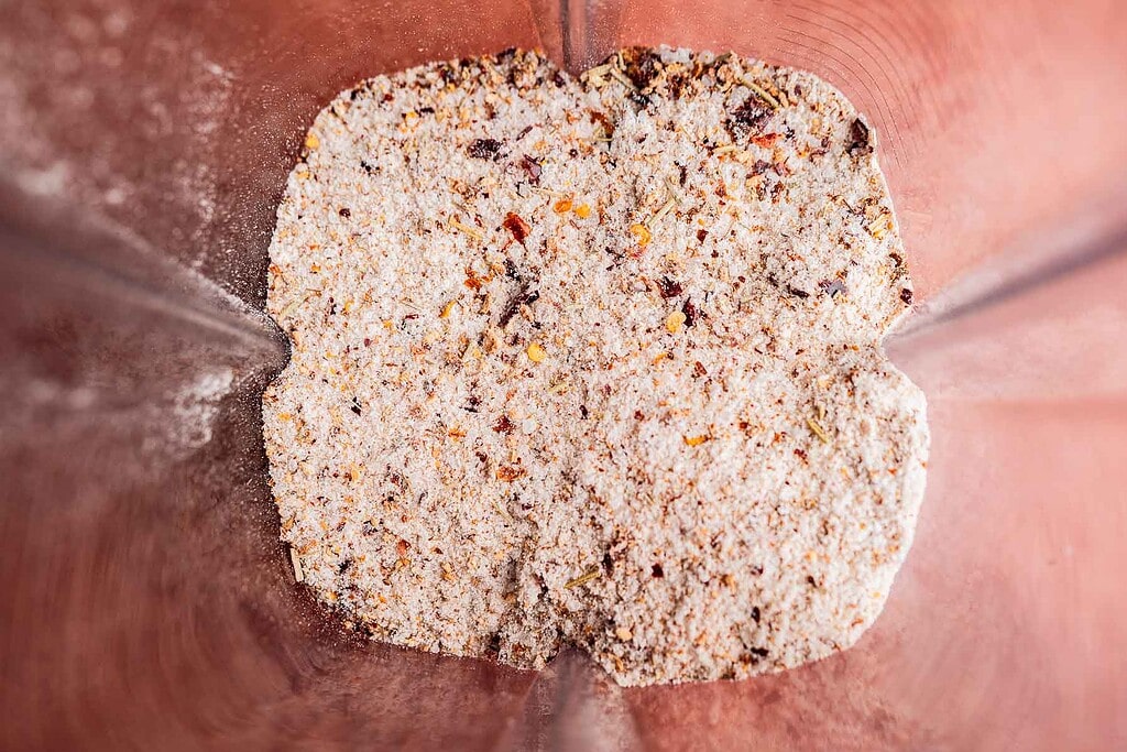 Ground dry ingredients and spicy salt in a blender, forming a coarse mixture with visible small pieces and specks of various colors.