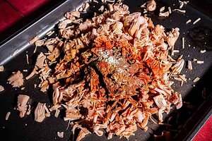 Shredded jackfruit, perfect for jackfruit birria, is topped with various spices on a dark baking tray, ready for cooking.