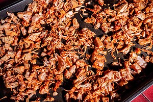 Seasoned, shredded jackfruit for jackfruit birria spread out on a dark baking tray, ready for roasting.