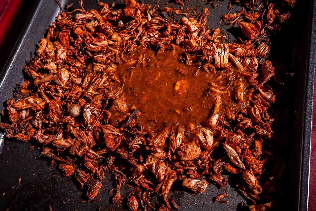 Shredded jackfruit birria with savory sauce on a baking tray.
