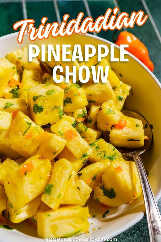A bowl of Trinidadian pineapple chow garnished with herbs and peppers, with a spoon resting inside. Text overlay reads "Trinidadian Pineapple Chow.