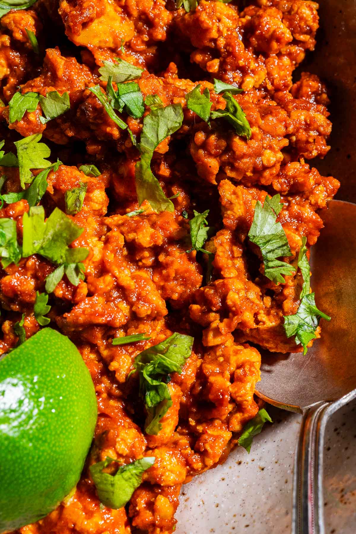 Close-up of spicy tofu sofritas garnished with chopped cilantro, with a lime wedge and a metal spoon beside the dish.