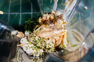A close-up of various fresh herbs, spices, creamy ingredients, and tofu ranch inside a blender, ready to be mixed.