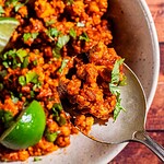 A close-up of a spoonful of seasoned sofritas ground meat garnished with chopped cilantro, with lime wedges visible in the bowl.