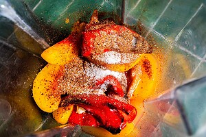 Sliced peaches and roasted red peppers with spices and sugar in a blender, ready to be blended.