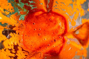 Bright orange-red sauce mixture seen from above inside a blender, with sauce splatters on the sides of the blender jar.