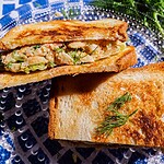 A toasted butter bean salad sandwich, filled with chicken salad and lettuce, is cut in half and served on a blue and white patterned plate, garnished with fresh dill.