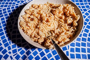 A bowl filled with mashed white beans for a butter bean salad sandwich sits beside a fork on a blue and white tiled surface.
