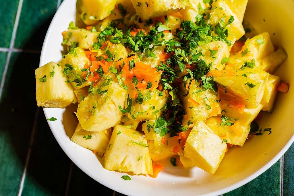 A white bowl filled with chopped yellow root vegetables garnished with chopped herbs, placed on a green tiled surface.