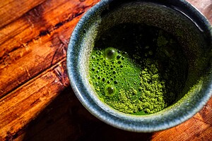 A ceramic cup with bright green matcha tea and visible powder on the surface, resting on a wooden table.