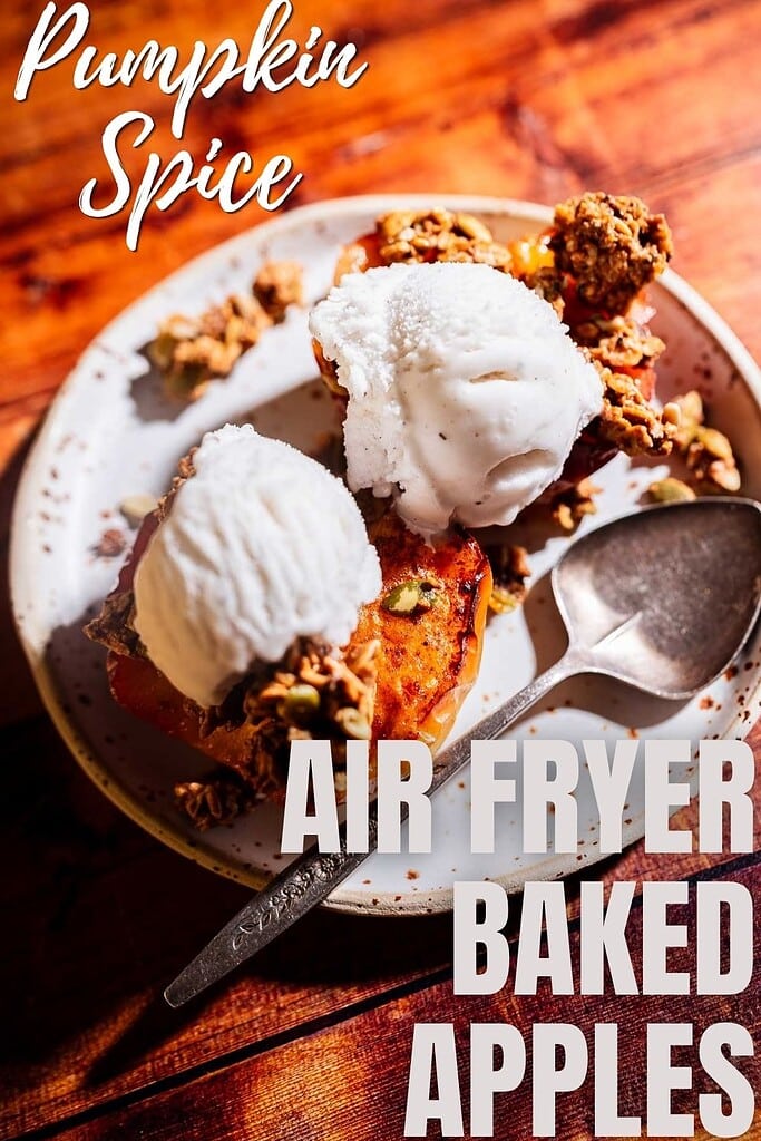 A plate with two baked apple halves topped with ice cream and granola, with a spoon on the side. Text reads “Pumpkin Spice Air Fryer Baked Apples.”.