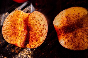 Two apple halves sprinkled with chili powder rest on a dark surface, with light highlighting the texture and spice.