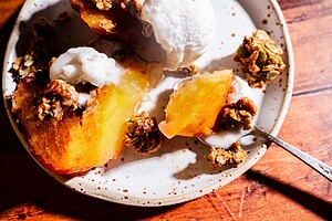 A plate with baked peach halves topped with granola and melting vanilla ice cream, set on a wooden table.