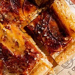 Close-up of a sliced caramel apple tart with flaky crust, caramelized apple slices, and a sprinkle of sea salt on brown parchment paper.
