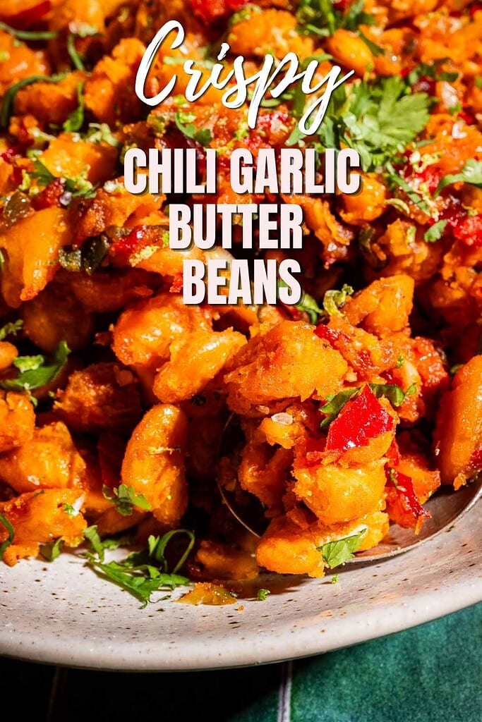 Close-up of a plate filled with crispy beans cooked with red chili, garlic, butter, and garnished with chopped fresh herbs. Text on image reads: “Crispy Chili Garlic Butter Beans.”.