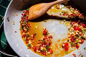 Chopped red and green peppers and garlic sauté in oil in a large pan with a wooden spoon.