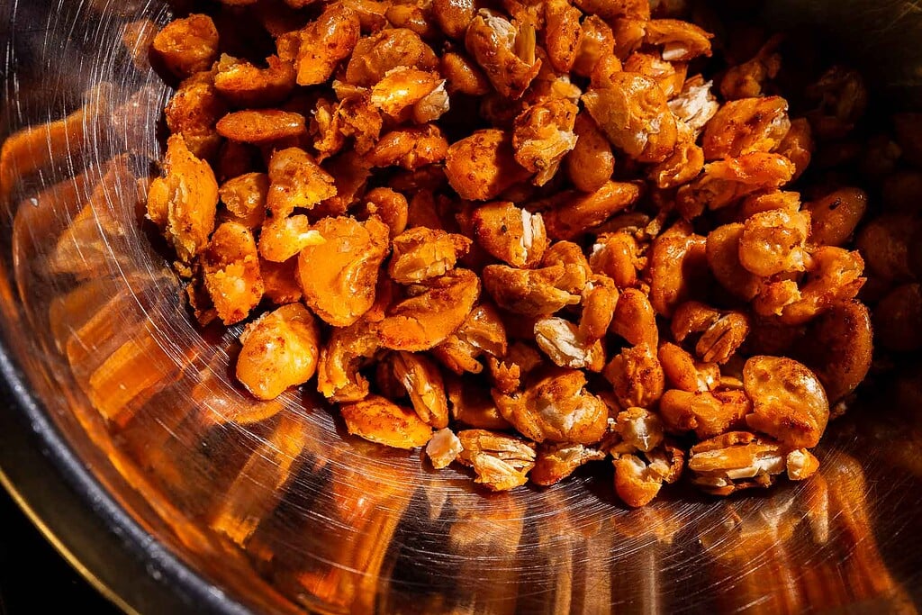 Close-up of a metal bowl filled with roasted, seasoned yellow split peas or lentils, some broken into pieces.