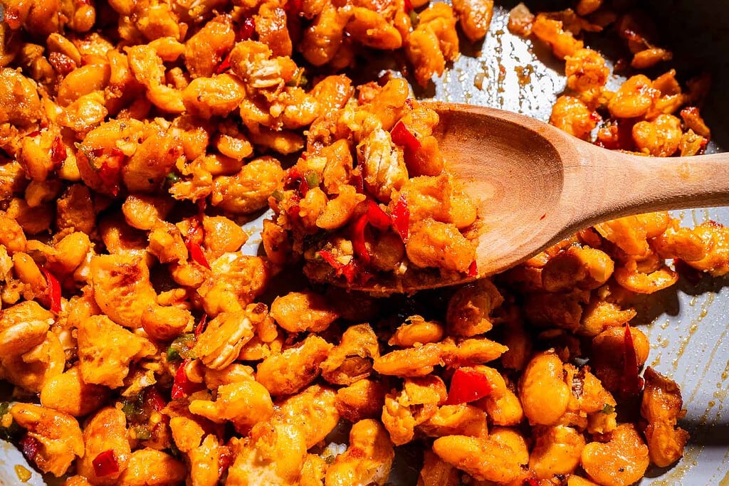 Cooked white beans with red peppers and spices in a pan, stirred with a wooden spoon.