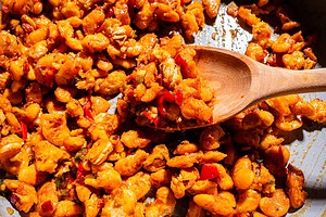 Cooked white beans with red peppers and spices in a pan, stirred with a wooden spoon.