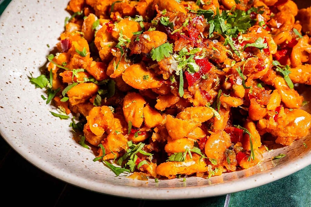 A close-up of a plate of cooked butter beans mixed with red peppers, onions, and garnished with fresh chopped cilantro.