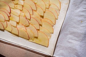 Thin apple slices arranged in overlapping rows on a sheet of pastry dough, placed on parchment paper and ready for baking—a delicious caramel apple tart in the making.