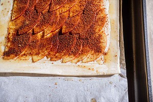A sheet of puff pastry topped with thinly sliced apples and a layer of cinnamon sugar, arranged on a baking sheet lined with parchment paper, creates the base for a delicious caramel apple tart.