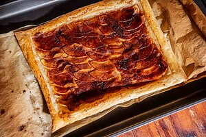 Rectangular caramel apple tart with thinly sliced apples on puff pastry, baked to golden perfection and placed on parchment paper in a baking tray.