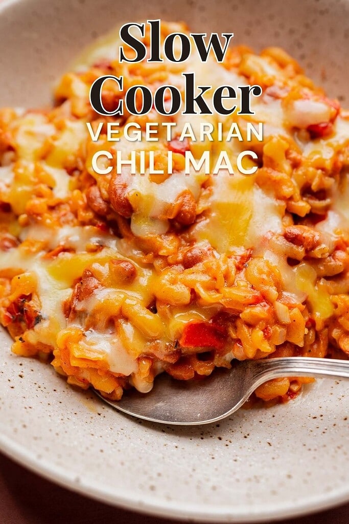 A plate of slow cooker chili mac with melted cheese, served with a spoon. Text overlay reads “Slow Cooker Vegetarian Chili Mac.”.