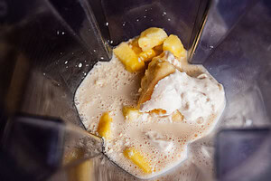 Blender with chunks of pineapple, a scoop of ice cream, and milk inside, ready to be blended into a delicious tropical smoothie.