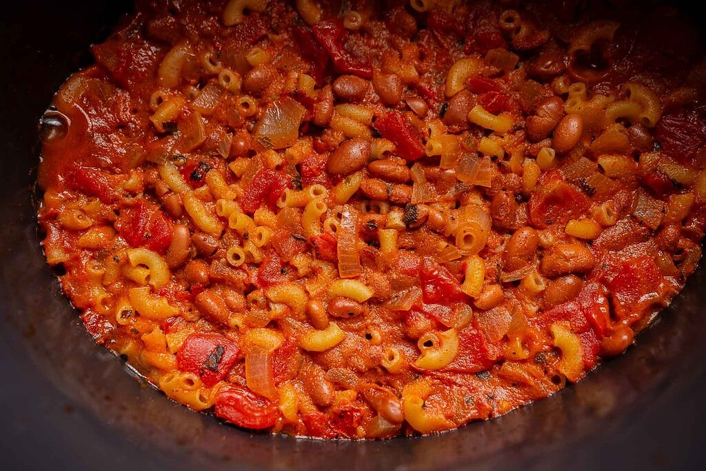 Close-up of cooked slow cooker chili mac with elbow macaroni, beans, diced tomatoes, and onions in a thick tomato-based sauce.