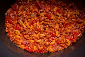 Close-up of cooked slow cooker chili mac with elbow macaroni, beans, diced tomatoes, and onions in a thick tomato-based sauce.