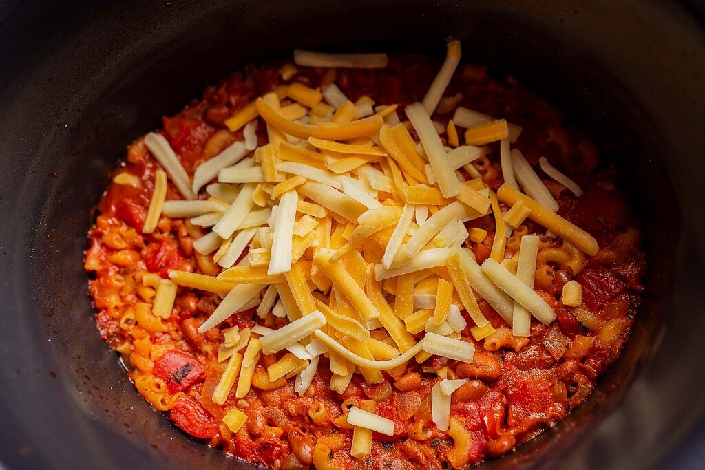 Macaroni with tomato sauce topped with shredded cheese in a black pot, reminiscent of a comforting slow cooker chili mac.