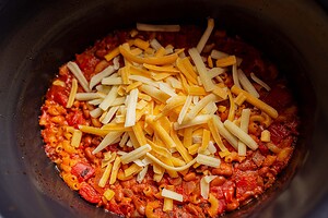 Macaroni with tomato sauce topped with shredded cheese in a black pot, reminiscent of a comforting slow cooker chili mac.