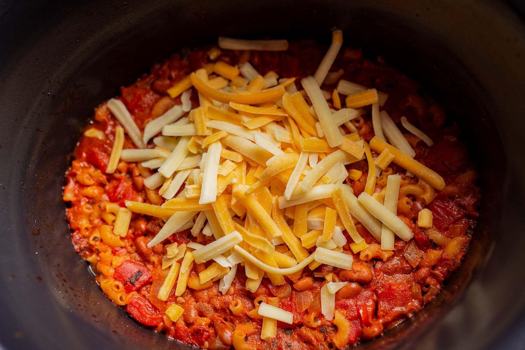 Macaroni with tomato sauce topped with shredded cheese in a black pot, reminiscent of a comforting slow cooker chili mac.