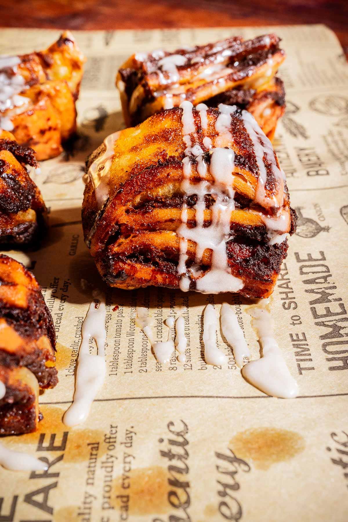 Close-up of a pumpkin spice pastry with icing drizzled on top, placed on parchment paper with printed text.
