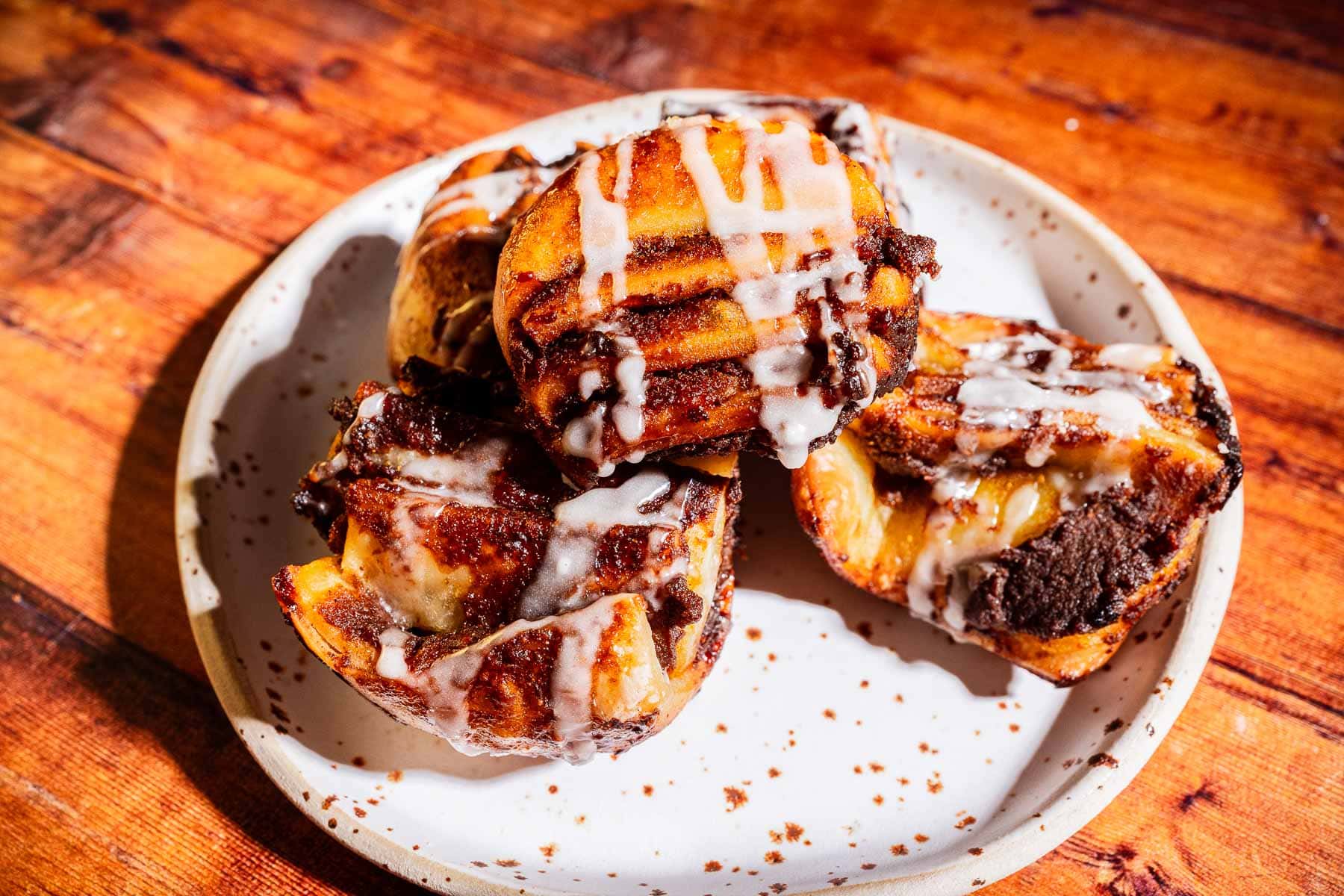 Four pumpkin puff pastries with icing are arranged on a white plate atop a wooden surface.