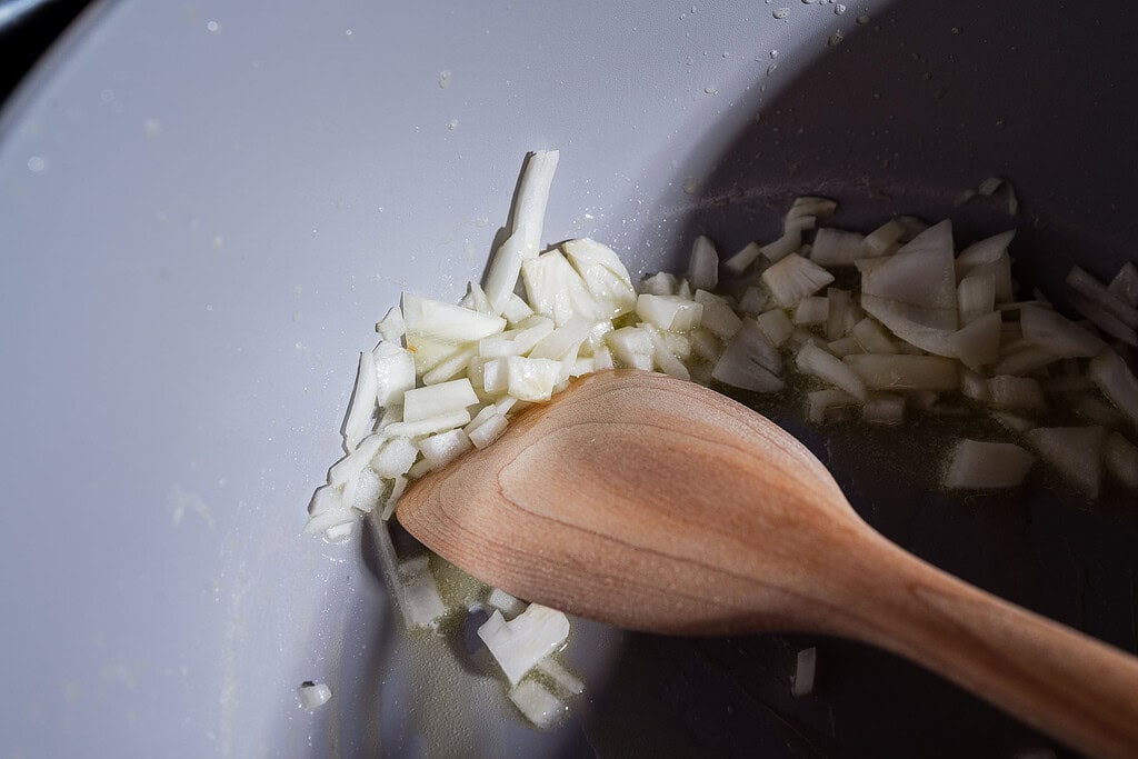 Chopped onions being sautéed in a pan with a wooden spoon, perfect as the aromatic base for a cozy pumpkin soup served in mini pumpkin bowls or crowned with golden puff pastry tops.