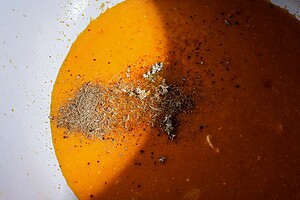 Orange liquid with piles of ground spices and minced garlic in a white bowl, partially covered by a shadow—perfectly reminiscent of creamy pumpkin soup, ready to be served in charming mini pumpkin bowls or topped with golden puff pastry tops.