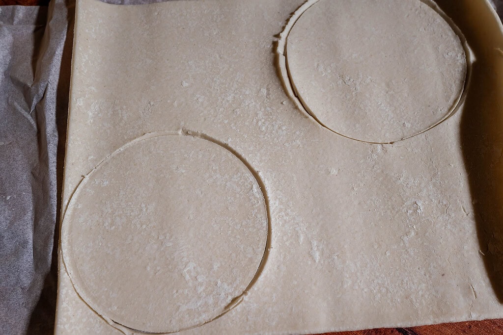 A sheet of pastry dough with two large circles cut out, perfect for creating puff pastry tops, placed on parchment paper.