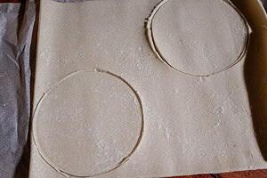 A sheet of pastry dough with two large circles cut out, perfect for creating puff pastry tops, placed on parchment paper.