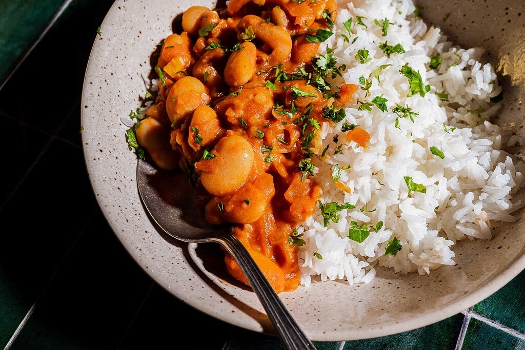 A plate of white rice and gochujang butter beans in tomato sauce, garnished with chopped parsley, with a spoon on the side.