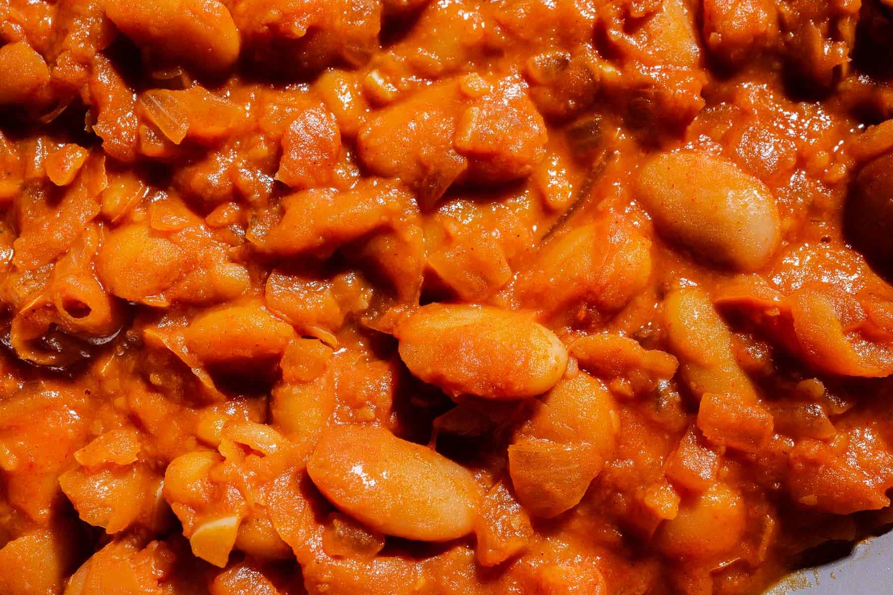 Close-up of gochujang butter beans cooked in a thick, orange-red tomato sauce with visible chunks of vegetables.
