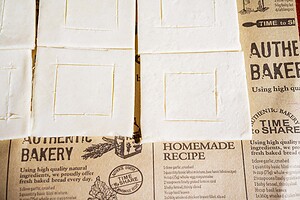 Sheets of raw hatch chile puff pastry with scored square shapes rest on brown paper with bakery-themed text and graphics.