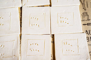 Several square pieces of uncooked hatch chile puff pastry dough with dotted and scored patterns are arranged on printed parchment paper.