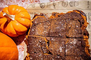 Sliced pumpkin bars with a chocolate topping and a sprinkle of salt, placed on parchment paper next to two small pumpkins—these treats are reminiscent of the popular date bark trend, blending comforting autumn flavors with a satisfying chocolatey finish.
