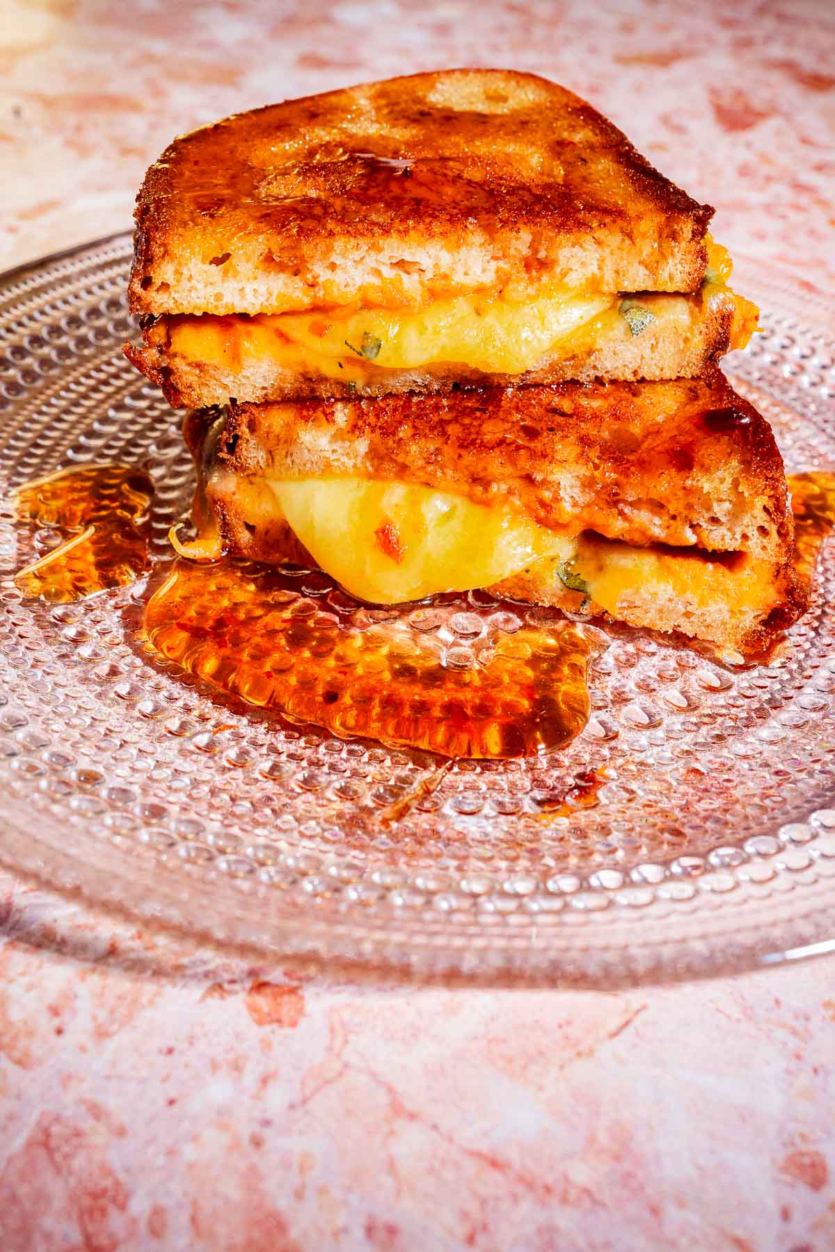 Two pumpkin grilled cheese sandwich halves stacked on a clear glass plate, with melted cheese and savory pumpkin filling oozing out and pooling onto the plate.